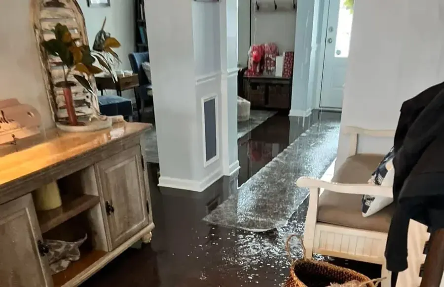 Standing water spread across a dark hardwood floor beside a cabinet